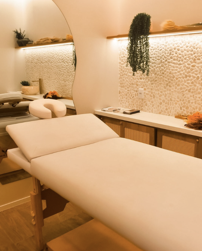 Sala de atendimento da clínica, com maca estofada, painel de pedras claras e prateleira com plantas